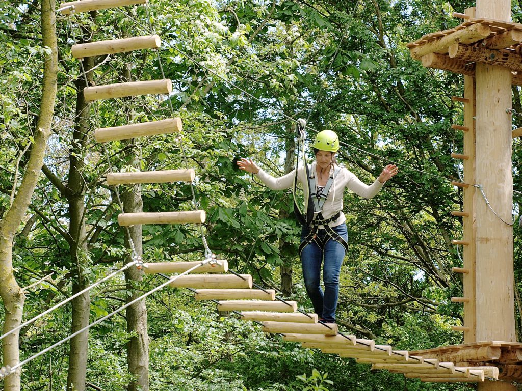 Mevrouw klimt over een wiebelbrug naar de trappen, in klimbos Klimpark Streekbos